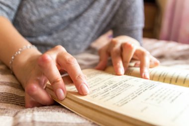 Romatizması olan genç bir kadın kitap okuyor. Elleri ve bacakları deforme olmuş. Acıyı hissediyor. Seçici odak.