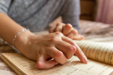 Romatizması olan genç bir kadın kitap okuyor. Elleri ve bacakları deforme olmuş. Acıyı hissediyor. Seçici odak.