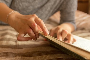 Romatizması olan genç bir kadın kitap okuyor. Elleri ve bacakları deforme olmuş. Acıyı hissediyor. Seçici odak.