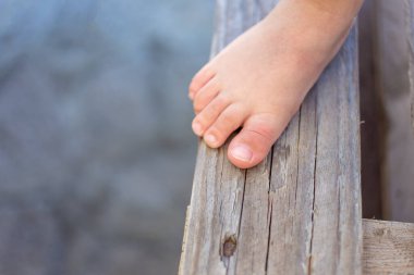 Yaz tatili sırasında havuzun yanındaki tahta zeminde duran küçük bir çocuğun bacakları. Seçici odak.