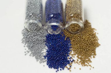 Cam kavanozlarda çok renkli boncuklar. Boncuklar beyaz bir ba üzerine dökülür