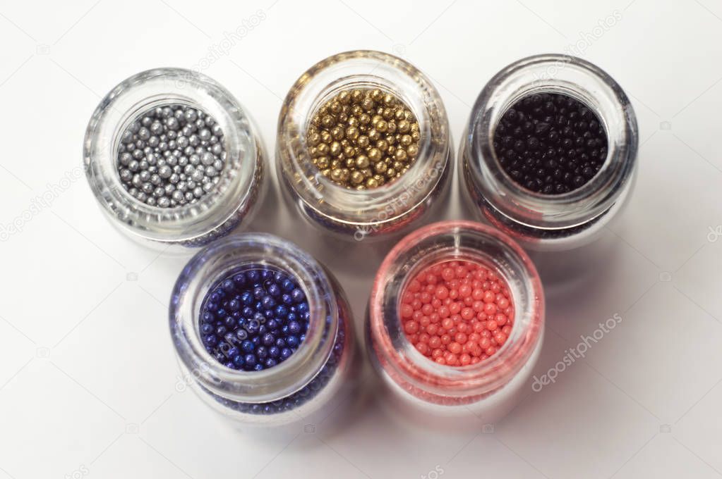 Multicolored beads in glass jars. Beads are poured on a white ba