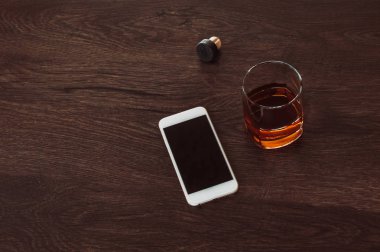 Viski, mantar ve cep telefonu ile cam ahşap bir masa üzerinde yalan.