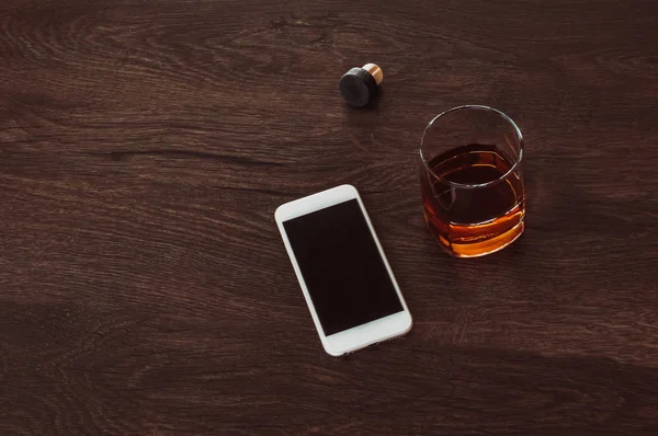 Bicchiere con whisky, sughero e telefono cellulare si trovano su un tavolo di legno . — Foto Stock