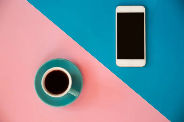 Una taza azul con café y un teléfono móvil se encuentra en un rosa y b —  Fotos de Stock
