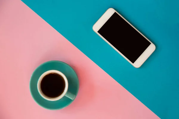 Una taza azul con café y un teléfono móvil se encuentra en un rosa y b —  Fotos de Stock