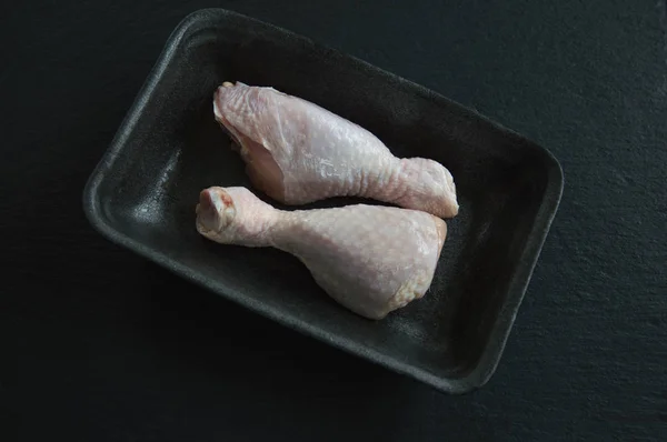 Two raw chicken legs lie in a plastic container on a black backg
