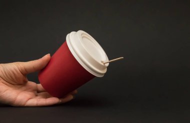 siyah bir arka plan üzerinde bir kapak ile kahve için kırmızı kağıt fincan, el 