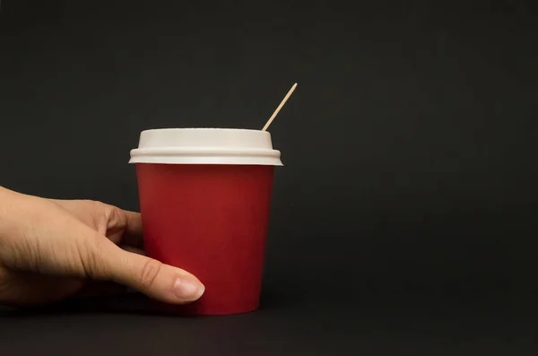 Rode papieren kop voor koffie met een deksel op een zwarte achtergrond, hand — Stockfoto