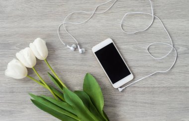 Beyaz kulaklık ve beyaz lale ile beyaz bir telefon bir w yatıyor