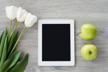 Beyaz çiçekli ve yeşil elmalı beyaz tablet beyaz bir elmanın üzerinde yatıyor.
