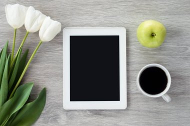 Beyaz çiçekli beyaz tablet, yeşil elma ve bir fincan kahve.