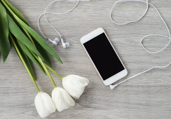 Белый телефон с белыми наушниками и белыми тюльпанами лежит на w — стоковое фото