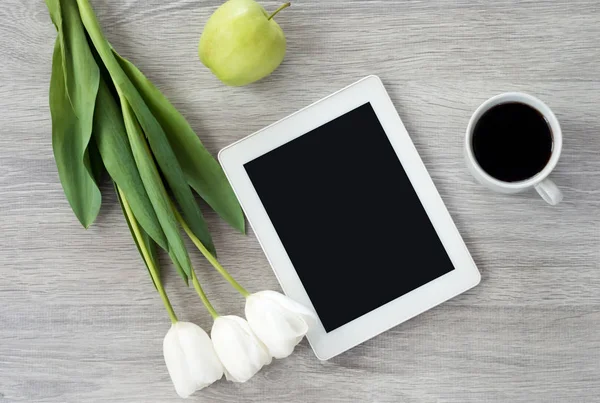 White tablet with white flowers, green apples and a cup of coffe