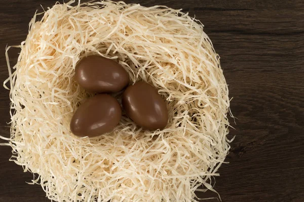 Easter. Chocolate eggs lie in a nest on a wooden brown table.