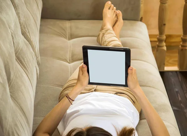 the girl is lying on the couch and reads news and messages on th