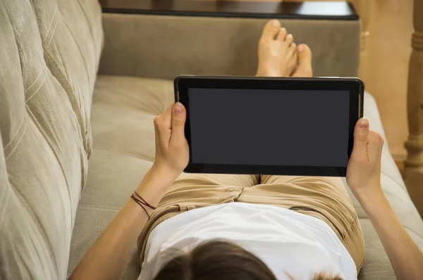 the girl is lying on the couch and reads news and messages on th