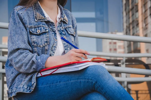 Девушка в джинсовой одежде сидит на скамейке, держит в руках тетради и бумажки. — стоковое фото