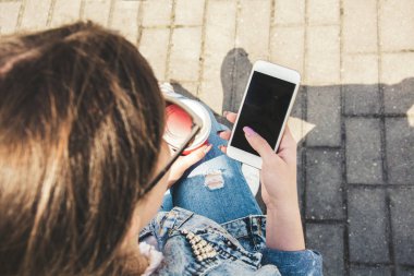 Kot ceketli genç bir kız sokakta kahveyle yürüyor.