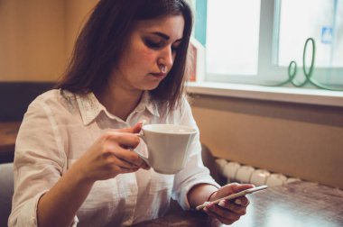 bir kafede kız kahve, çay içecekler ve telefona bakar, okumak