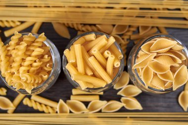 Tahta bir masada çiğ makarna. Yukarıdan manzara. Spagetti, lazanya, fusilli, besbarmak erişte.