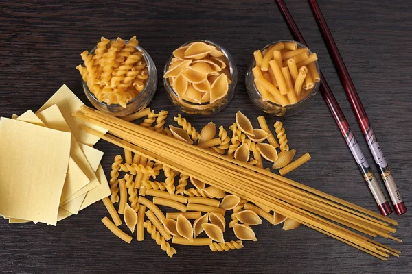 Tahta bir masada çiğ makarna. Yukarıdan manzara. Spagetti, lazanya, fusilli, besbarmak erişte.