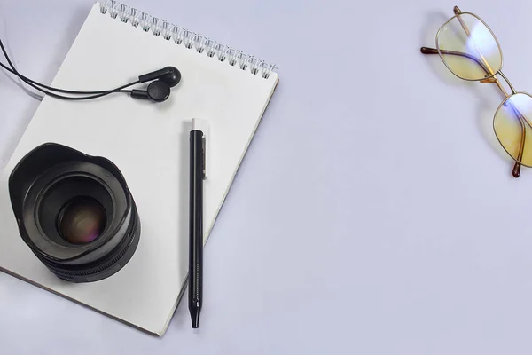 White photographer\'s Desk with notebook, lens, pen, glasses.