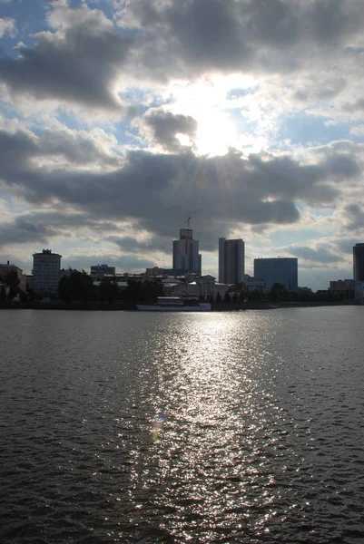 川の近くの建物の上に雲を通って来る太陽の光 — ストック写真