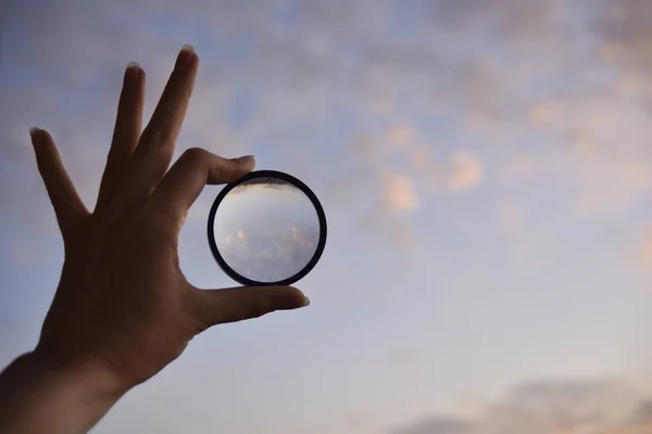 Silhouette einer weiblichen Hand, die die Linse und den Himmel auf dem Hintergrund zum Zeitpunkt des Sonnenuntergangs hält — Stockfoto