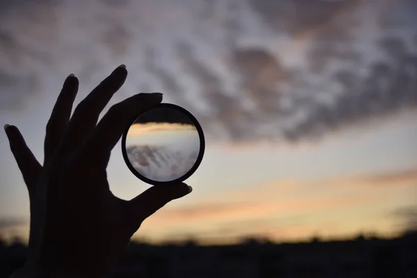 Silhouet van de vrouwelijke hand houden de lens en de hemel op de achtergrond op het moment van de zonsondergang — Stockfoto
