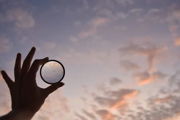 Silhouet van de vrouwelijke hand houden de lens en de hemel op de achtergrond op het moment van de zonsondergang — Stockfoto
