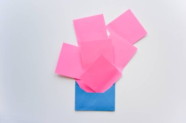 seçici odak, kaos içindeki pembe kağıt çıkartmaları ve beyaz arka planda mavi zarf.