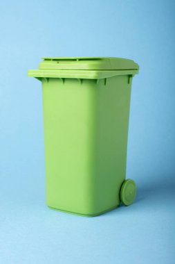 Mavi arka planda yeşil çöp kovası. Geri dönüşüm. Mavi arka planda geri dönüşüm ve yeniden kullanım için malzemeler. Ekolojik kavram, konteynırlarda birçok geri dönüşümlü nesne