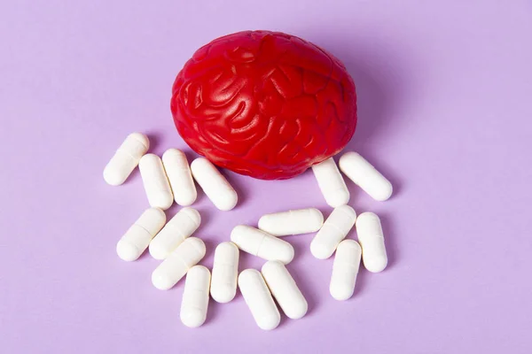 Red brain on a pink background with white pills. Some pills for the brain. Symbolic for drugs, psychopharmaceuticals, nootropics and other drugs. The medicine. Brain treatment