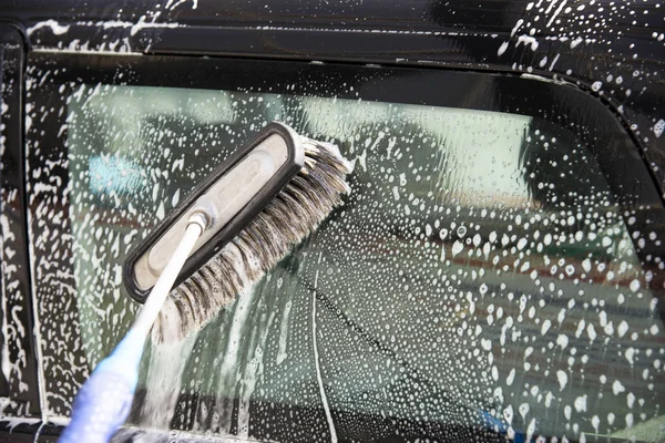 Side window of a black car wash in a car wash. Brush strokes are visible on the glass in white shampoo and foam