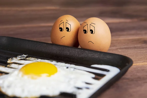 Eggs with a sad face near a fried egg. Humorous picture