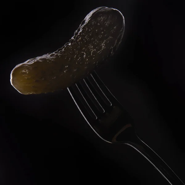 Солоний огірок на виделці на чорному тлі — стокове фото