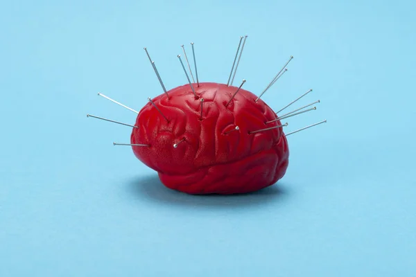 Red brain on a blue background with injected needles. Brain control concept. Brain treatment
