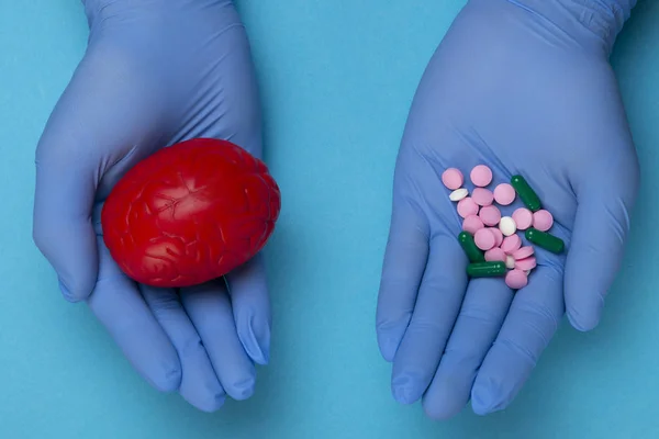 3D anatomical model of the brain and pink and blue pills on the palm on a blue background. Medical concept for a pharmacological pill for the treatment of brain diseases, pharmacotherapy, chemotherapy