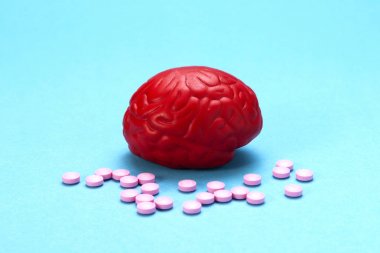 Pembe haplarla mavi arka planda kırmızı beyin. Beyin için bazı haplar. Bu ilaçlar, psikofarmasötikler, nootropics ve diğer ilaçlar için sembolik. İlaç. Beyin tedavisi
