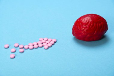 Pembe haplarla mavi arka planda kırmızı beyin. Beyin için bazı haplar. Bu ilaçlar, psikofarmasötikler, nootropics ve diğer ilaçlar için sembolik. İlaç. Beyin tedavisi