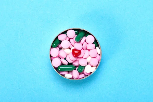 Pequeno coração vermelho com pílulas multi-coloridas em um fundo azul — Fotografia de Stock