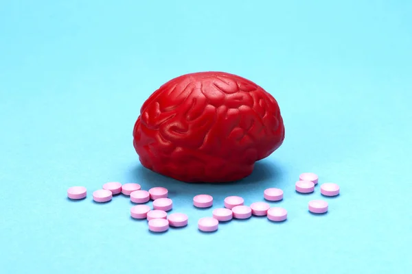Cerebro rojo sobre fondo azul con pastillas rosas. Unas pastillas para el cerebro. Es simbólico para las drogas, psicofármacos, nootrópicos y otras drogas. La medicina. Tratamiento cerebral — Foto de Stock