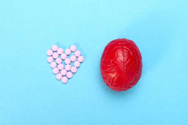 Cérebro vermelho num fundo azul com comprimidos cor de rosa. Alguns comprimidos para o cérebro. É simbólica para drogas, psicofármacos, nootrópicos e outras drogas. O remédio. Tratamento cerebral — Fotografia de Stock