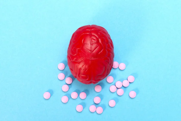 Cérebro vermelho num fundo azul com comprimidos cor de rosa. Alguns comprimidos para o cérebro. É simbólica para drogas, psicofármacos, nootrópicos e outras drogas. O remédio. Tratamento cerebral — Fotografia de Stock