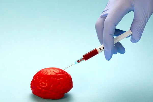 Red brain on a blue background. An unknown drug is injected into the brain. The injection is made by hand using a blue latex glove