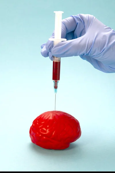 Red brain on a blue background. An unknown drug is injected into the brain. The injection is made by hand using a blue latex glove
