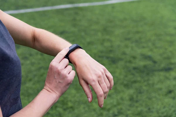 Female hand with smart watch on green outdoor sports stadium background