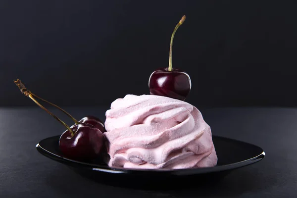 Bolo rosa doce com uma única cereja no topo em um pires preto contra um fundo escuro. Marshmallows de cereja rosa — Fotografia de Stock