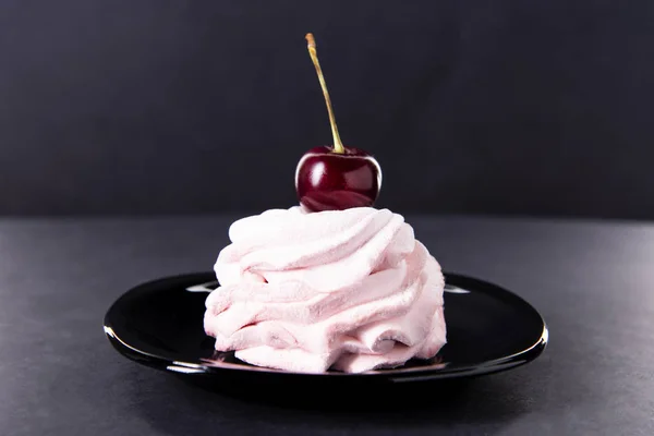 Bolo rosa doce com uma única cereja no topo em um pires preto contra um fundo escuro. Marshmallows de cereja rosa . — Fotografia de Stock